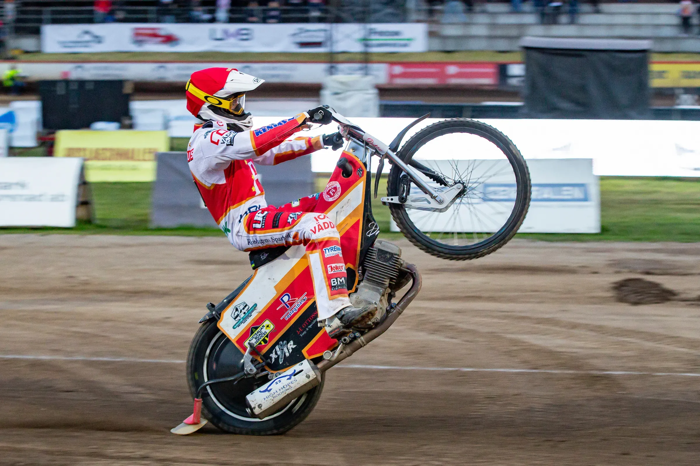 Speedwayförare som lyfter framhjulet på grusbanan.