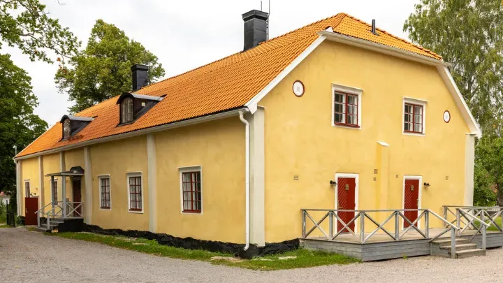 Flygeln Paradiset med gul träfasad, vita fönster och grönskande omgivning.