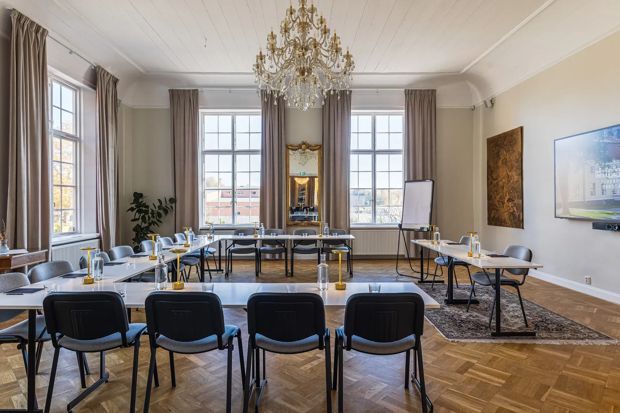 Konferenslokal med långbord, kristallkrona och fönster mot parken.