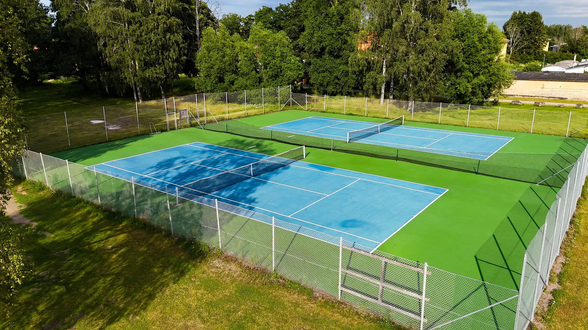 Två tennisbanor omgivna av grönska, sedda uppifrån.