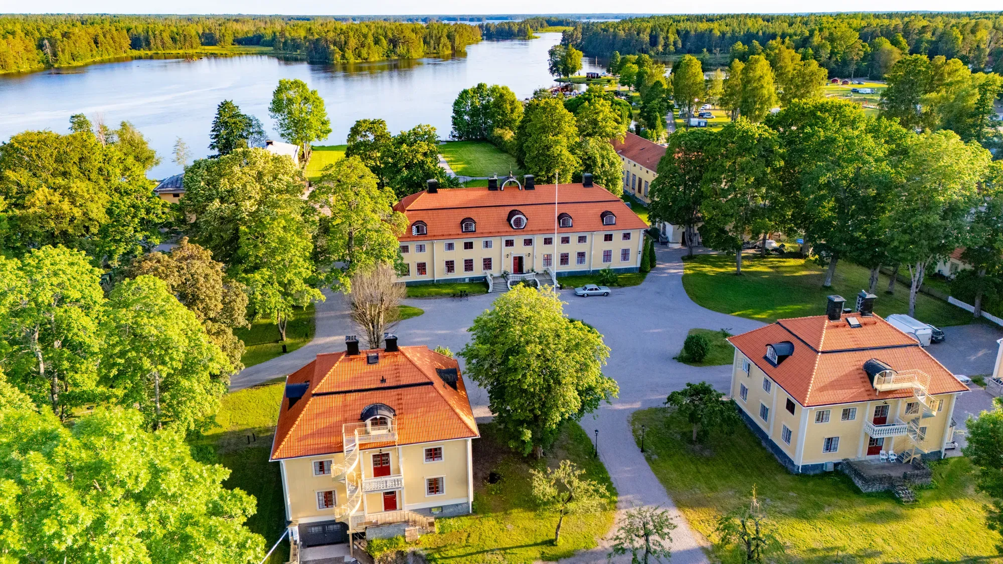 Söderfors Herrgårds gula byggnader med tegeltak, omgivna av grönska vid Dalälven.