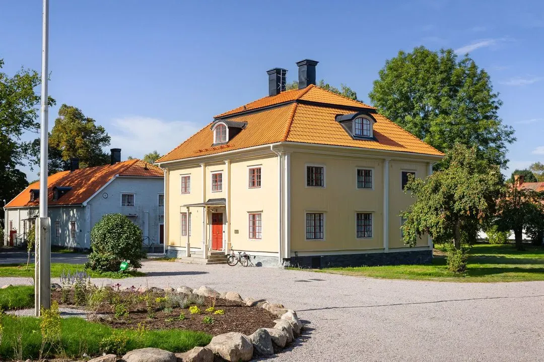 Brukshusets gula fasad och entré omgivna av herrgårdens planteringar.