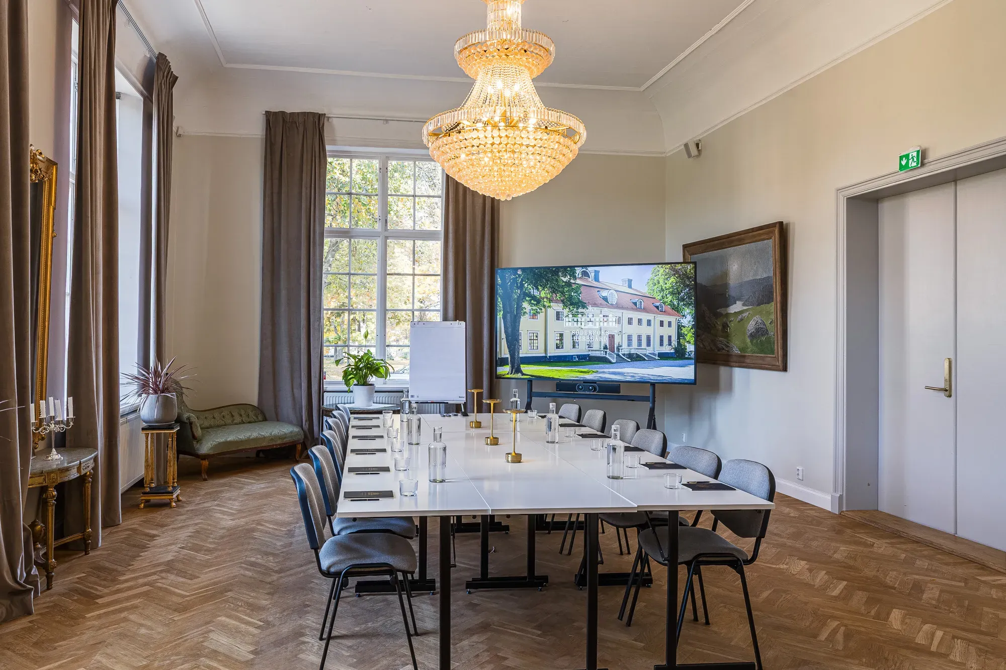 Konferenslokal med långbord, kristallkrona och fönster mot parken.