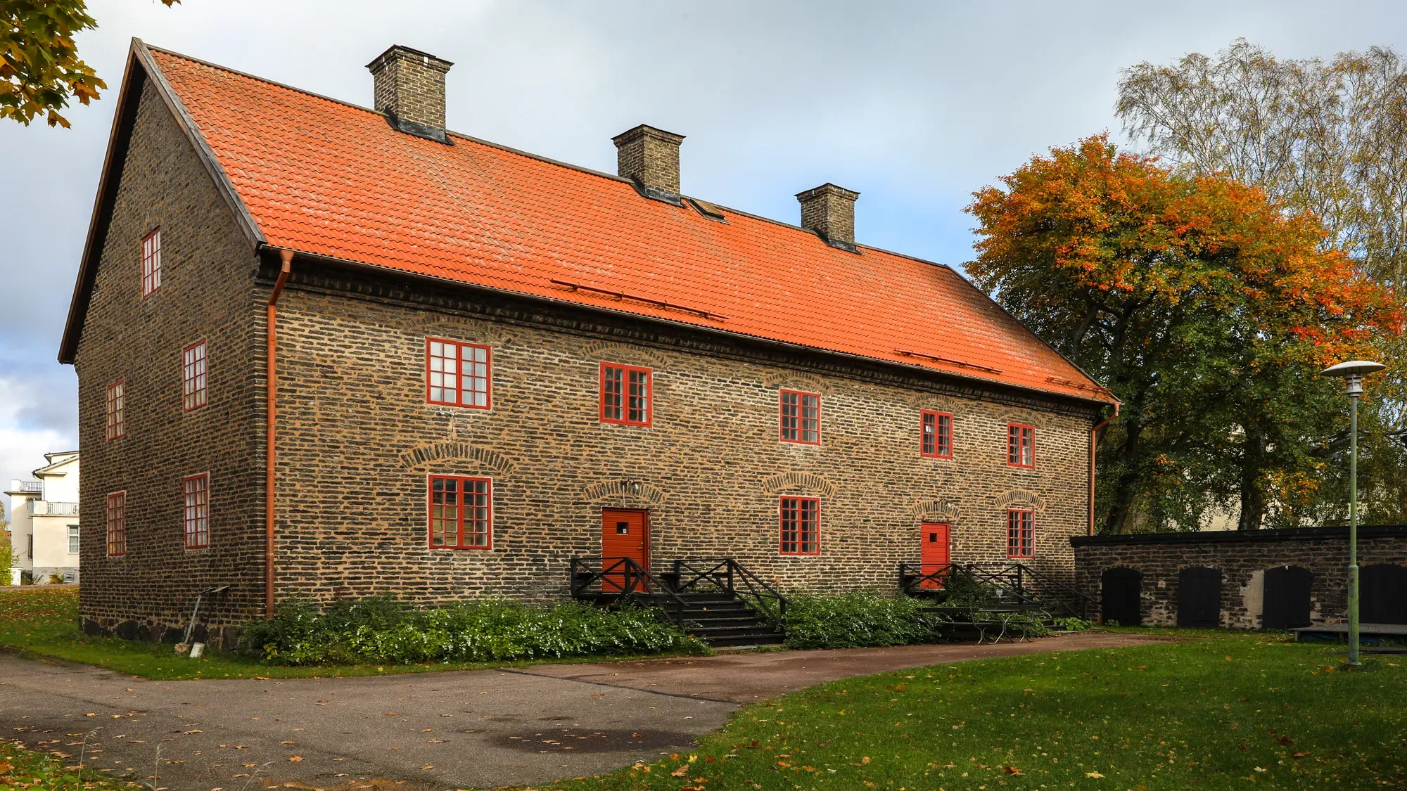 Änkehusets långa stenfasad med rött tegeltak och röda dörrar.