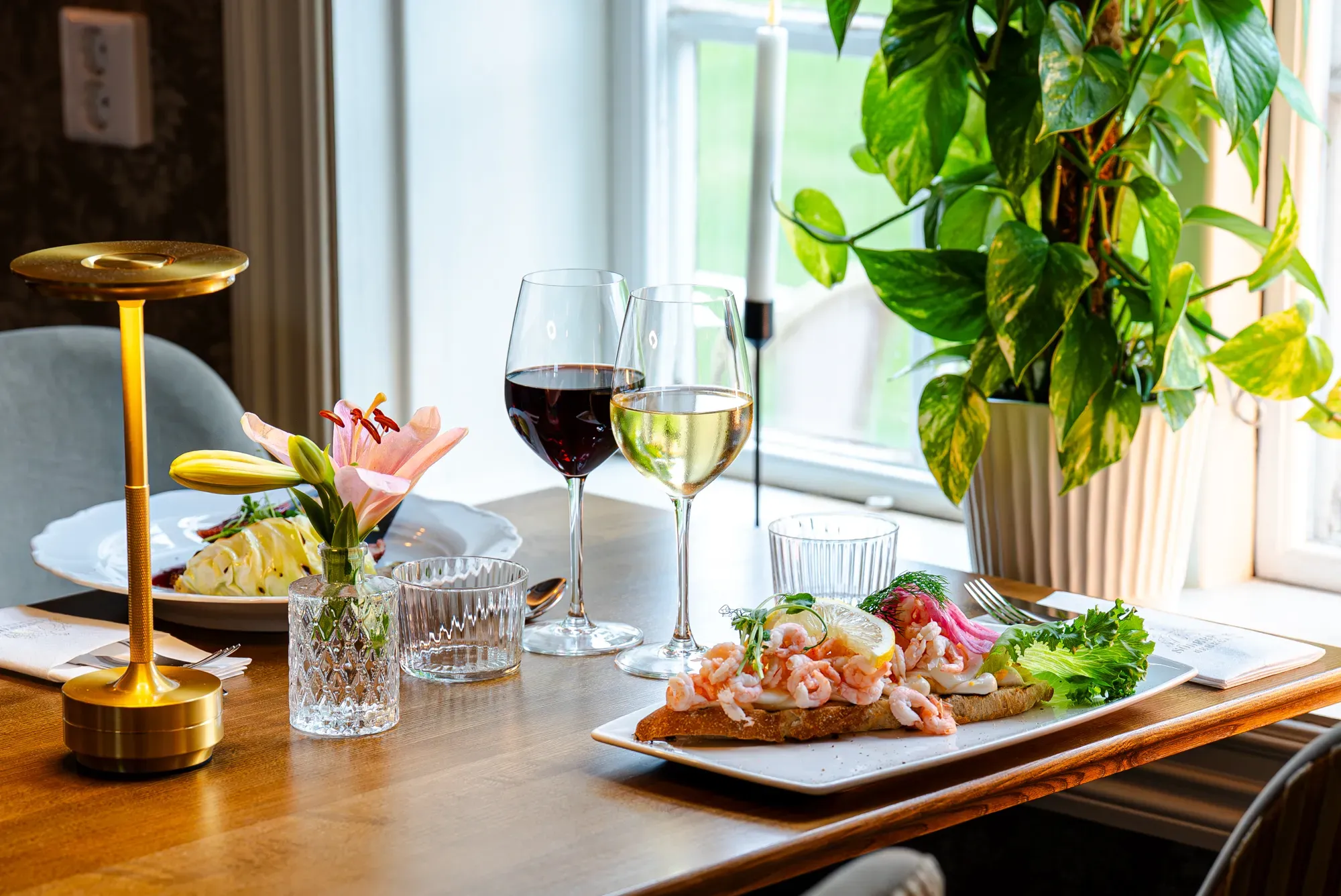 Smörgåsar med räkor, vin och blommor uppdukade vid ett fönster i restaurangen.