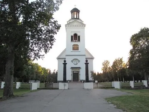 Söderfors kyrkas ljusa fasad och torn omgivet av grönska nära herrgården.