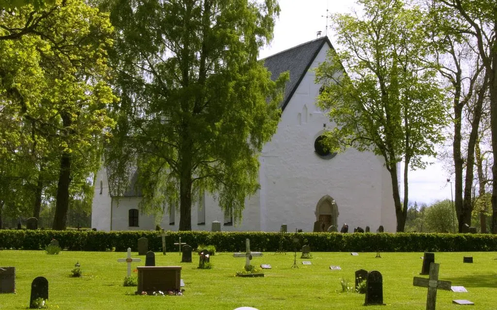Tierps vitputsade kyrka bakom kyrkogårdens gravstenar.