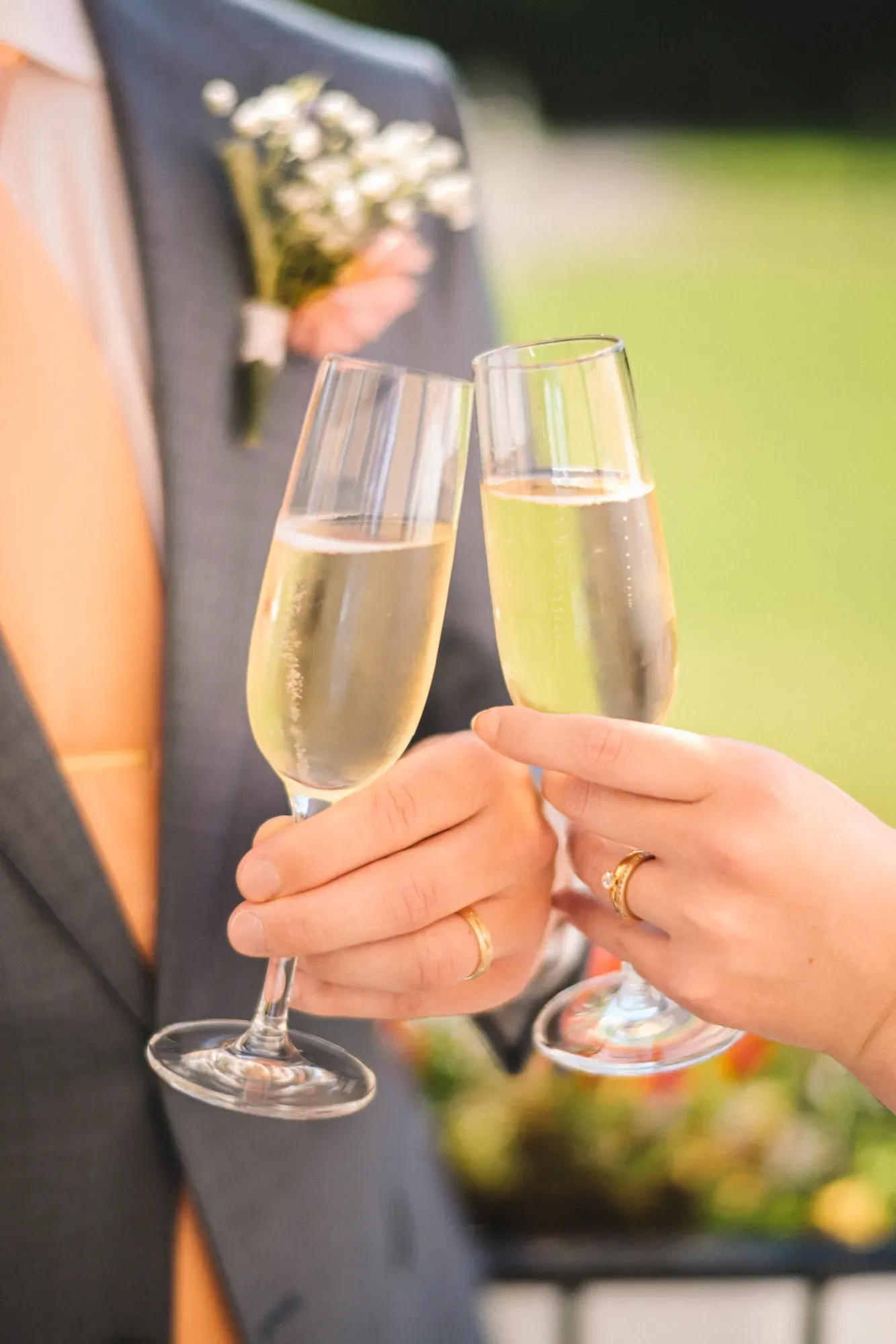 Brudparet skålar i champagne utomhus, med vigselringarna på händerna.